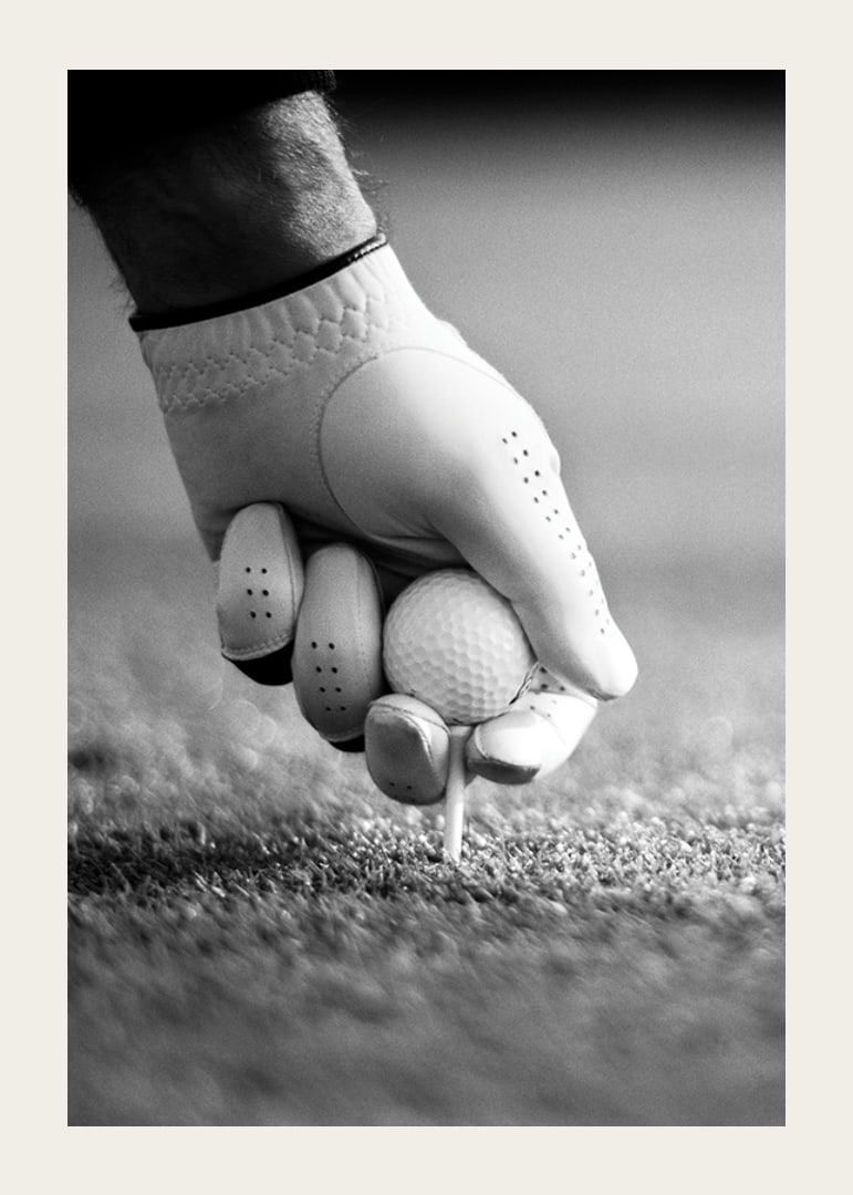 Black and white close-up of hand with golf glove placing ball on tee-12