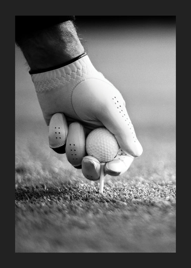 Svart-hvitt nærbilde av hånd med golfhanske som plasserer ballen på tee-12