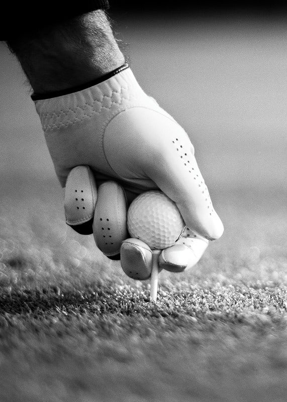 Black and white close-up of hand with golf glove placing ball on tee-12