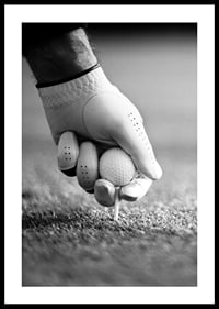 Black and white close-up of hand with golf glove placing ball on tee-0