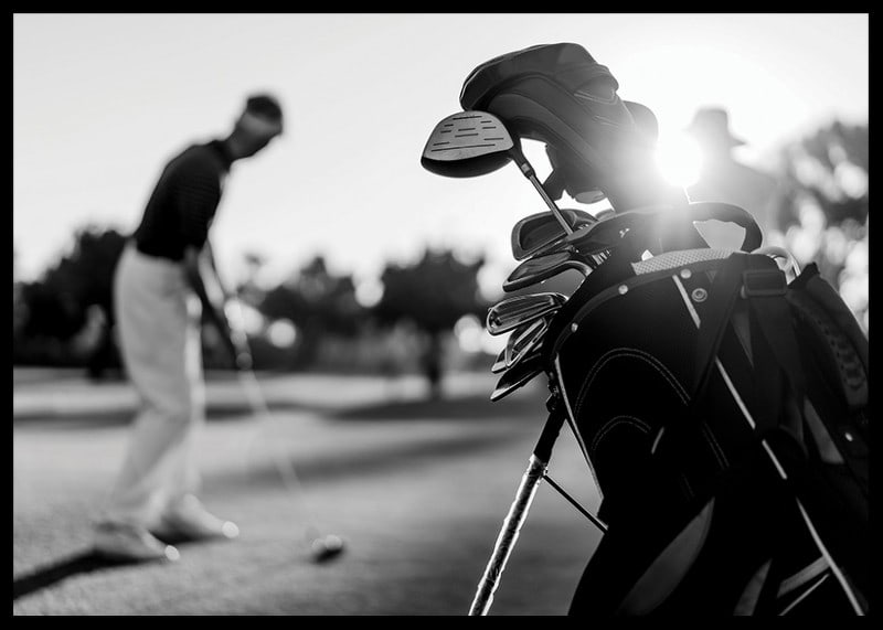 Svart-hvitt-bilde av golfbag i fokus, uskarp golfspiller bak-12