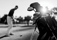 Svart-hvitt-bilde av golfbag i fokus, uskarp golfspiller bak-7