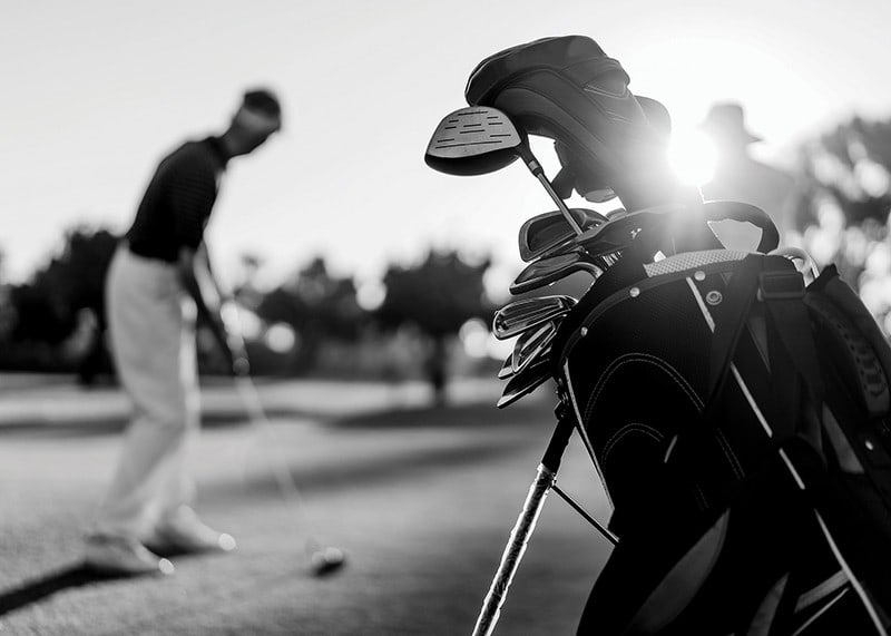 Svart-hvitt-bilde av golfbag i fokus, uskarp golfspiller bak-12