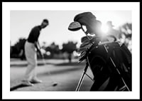 Svart-hvitt-bilde av golfbag i fokus, uskarp golfspiller bak-0