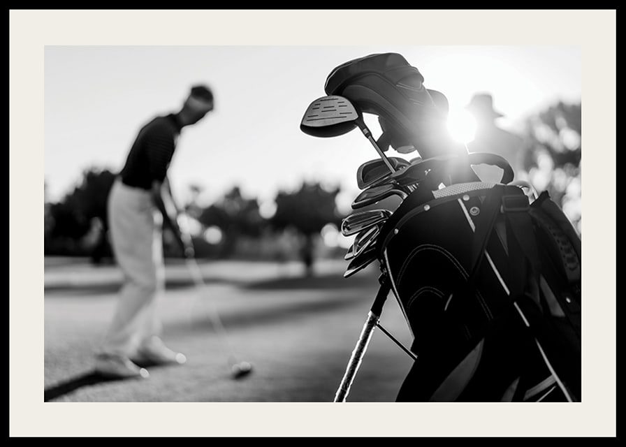 Svart-hvitt-bilde av golfbag i fokus, uskarp golfspiller bak-12