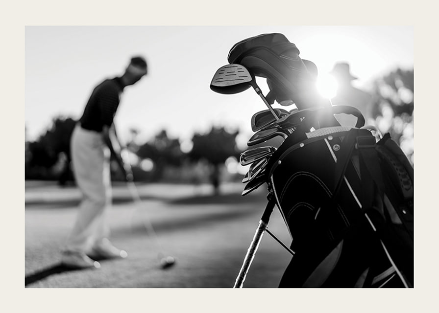 Svart-hvitt-bilde av golfbag i fokus, uskarp golfspiller bak-12