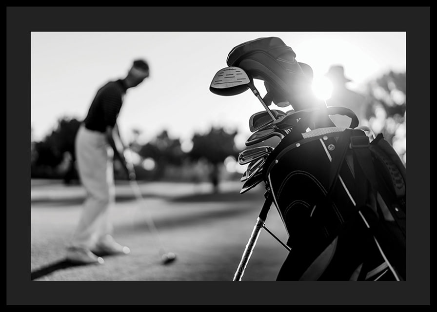 Svart-hvitt-bilde av golfbag i fokus, uskarp golfspiller bak-12