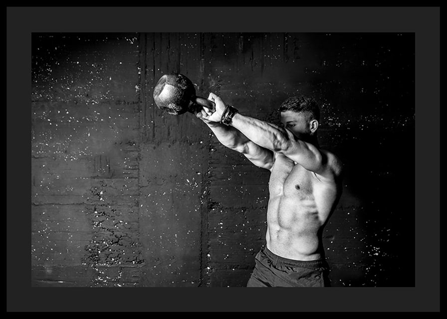 Black and white close-up of man exercising with kettlebell against raw concrete wall-12