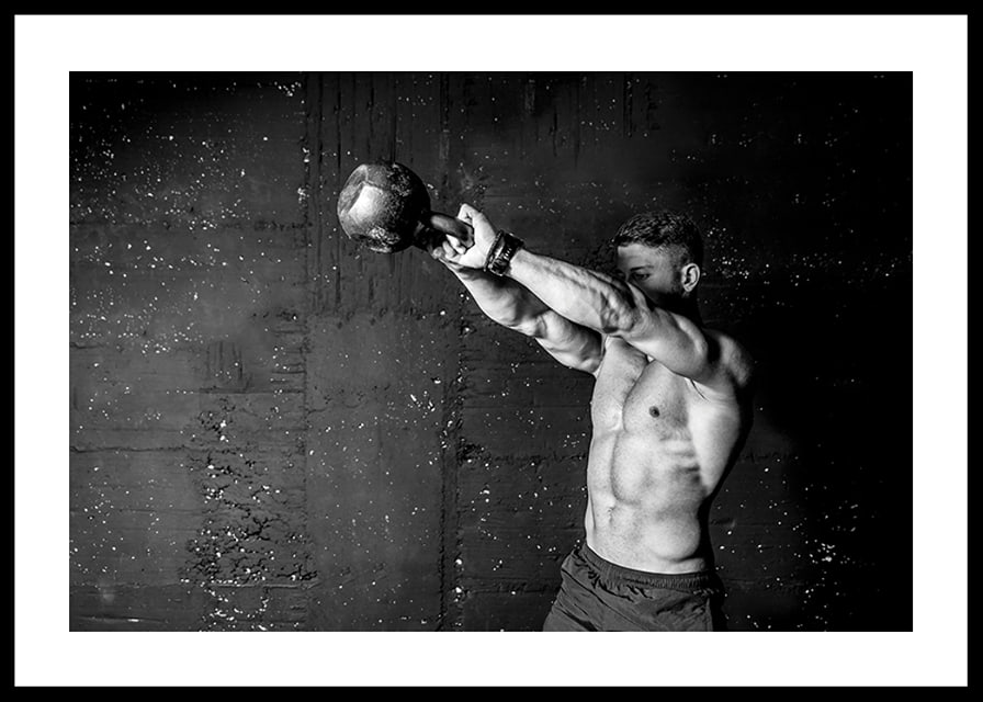 Black and white close-up of man exercising with kettlebell against raw concrete wall-12