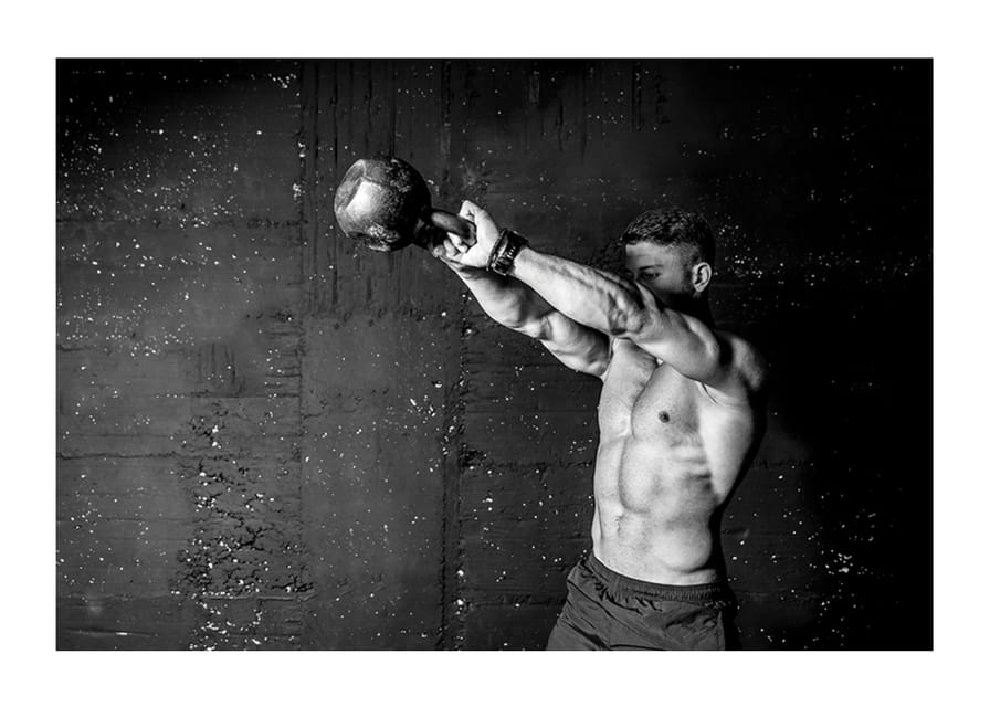 Gros plan noir et blanc d'un homme faisant de l'exercice avec une kettlebell contre un mur en béton brut-12