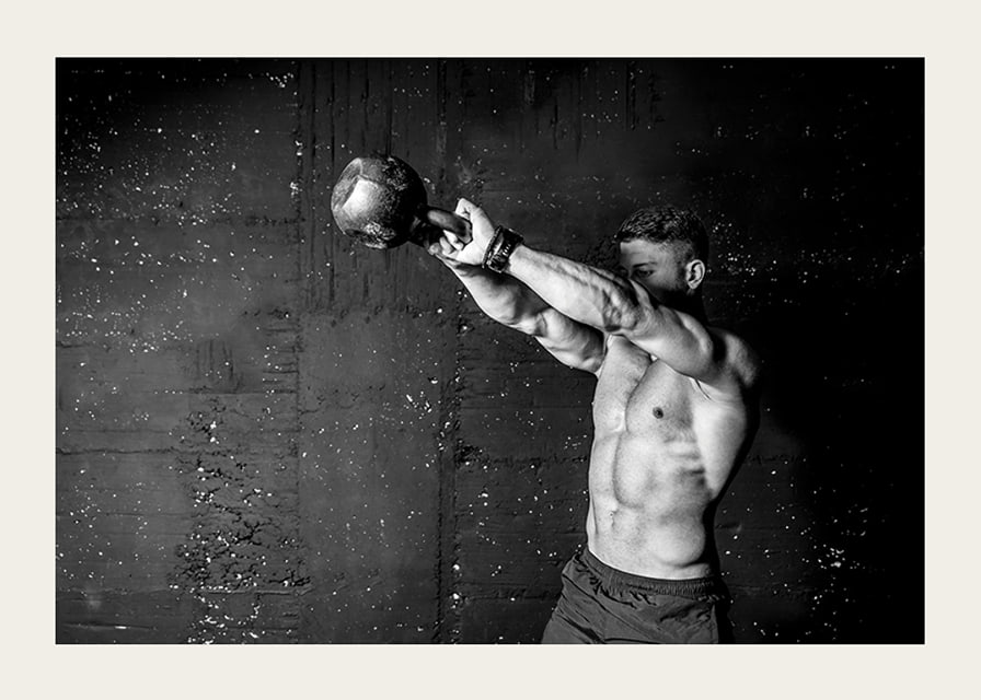 Black and white close-up of man exercising with kettlebell against raw concrete wall-12