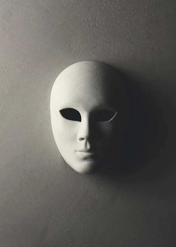 White theater mask with smooth features against gray wall in shadowy light-12