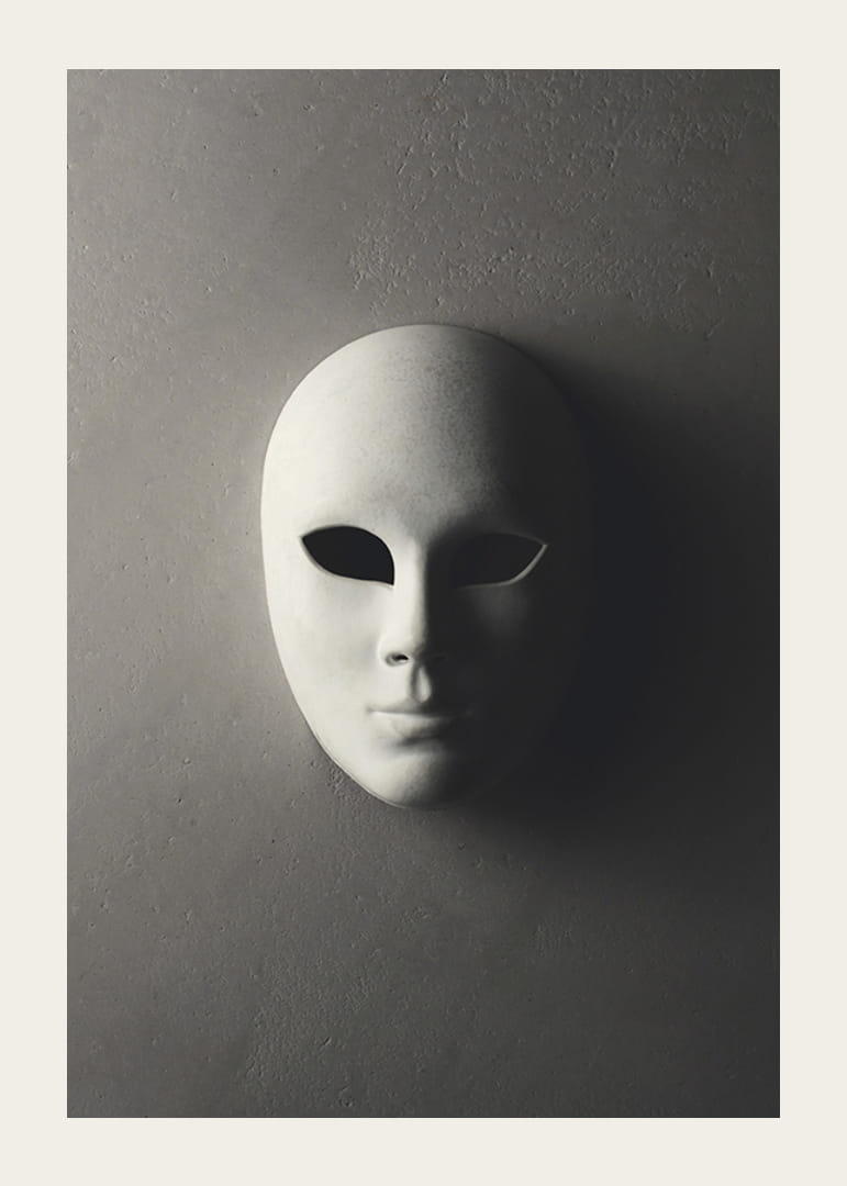 Maschera teatrale bianca con lineamenti lisci contro un muro grigio in una luce ombrosa-12