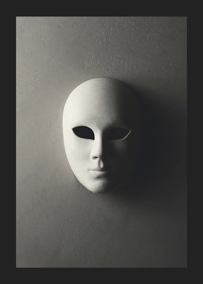 White theater mask with smooth features against gray wall in shadowy light-12