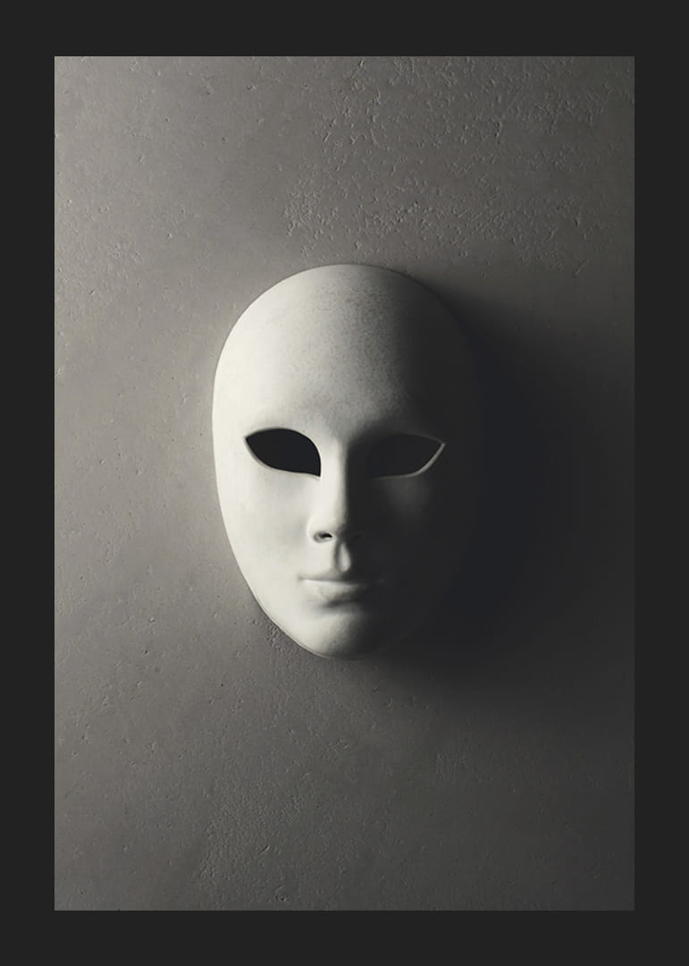 Maschera teatrale bianca con lineamenti lisci contro un muro grigio in una luce ombrosa-12