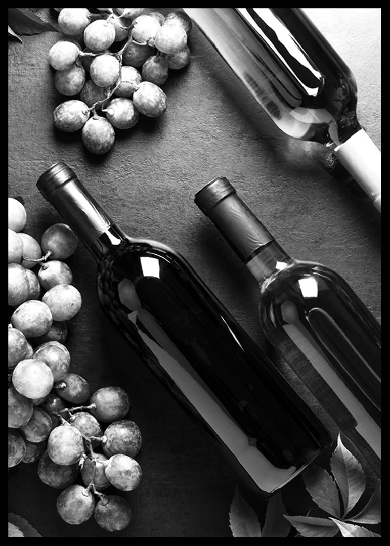 Black and white close-up of wine bottles and bunches of grapes on dark surface-12