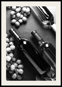 Black and white close-up of wine bottles and bunches of grapes on dark surface-2