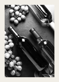 Black and white close-up of wine bottles and bunches of grapes on dark surface-3