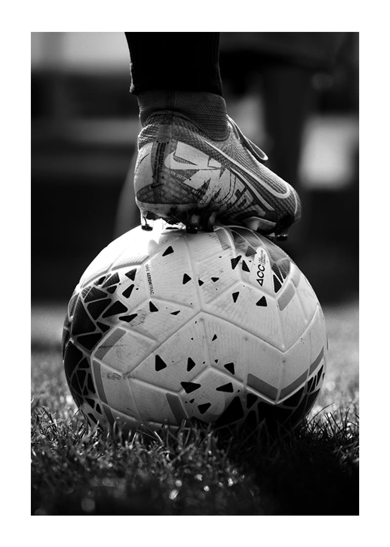 Black and white photo of soccer shoe placed on a football-12