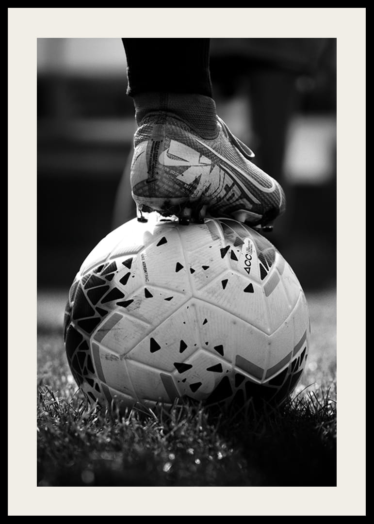 Black and white photo of soccer shoe placed on a football-12