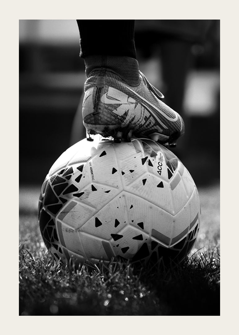 Fekete-fehér fotó egy futballcipőről, amelyet egy focilabda lábára helyeztek-12