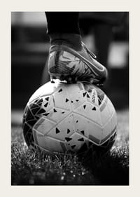 Black and white photo of soccer shoe placed on a football-5