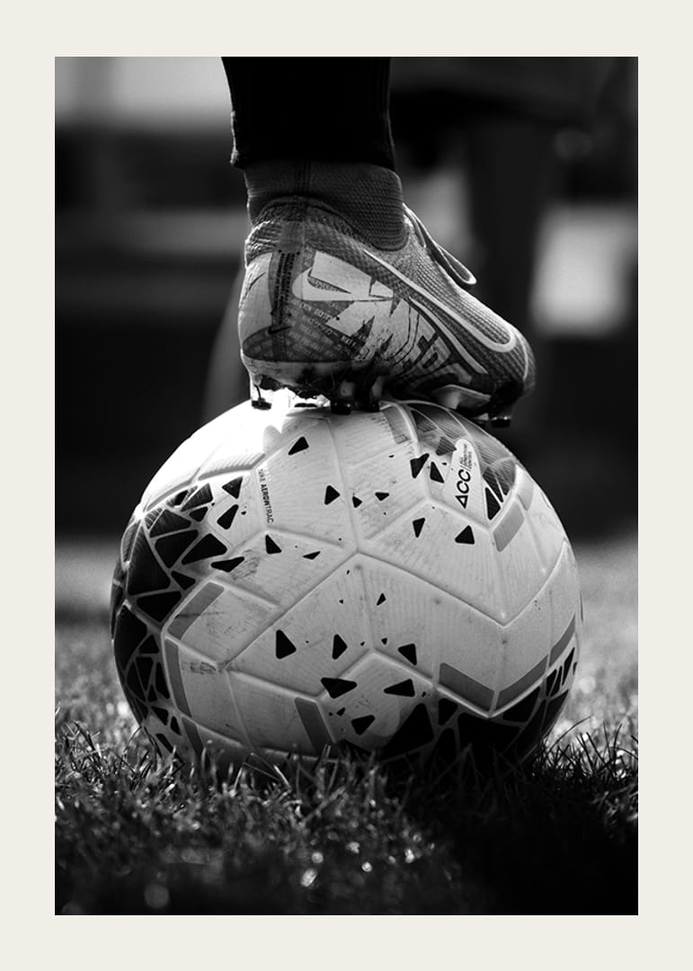 Black and white photo of soccer shoe placed on a football-12