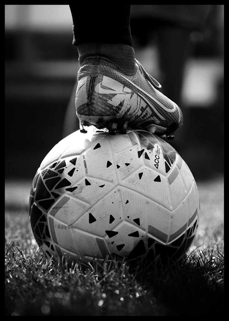 Fekete-fehér fotó egy futballcipőről, amelyet egy focilabda lábára helyeztek-12