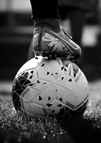 Fekete-fehér fotó egy futballcipőről, amelyet egy focilabda lábára helyeztek-7