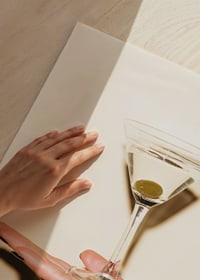 Fotografi av martiniglas med oliv på hand mot beige bakgrund-3