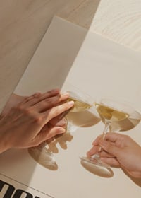 Twee handen houden martiniglazen met olijven vast tegen een beige achtergrond-3