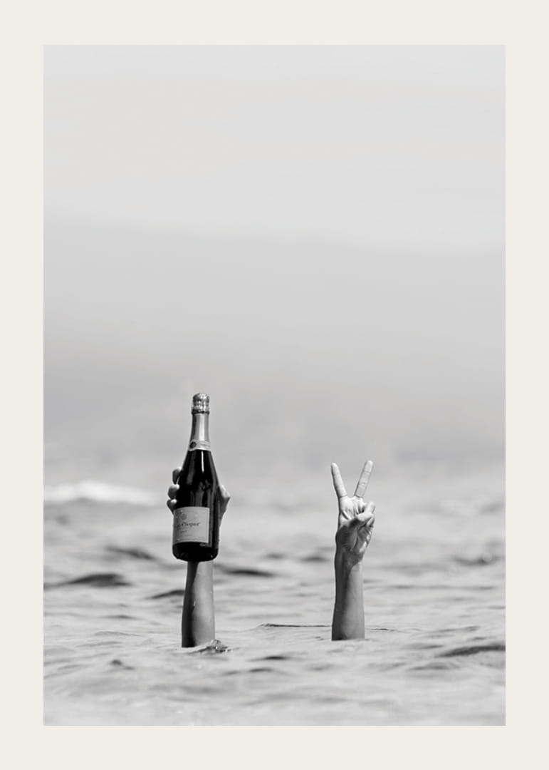 Svartvitt fotografi med två armar i vatten, en håller champagne-12