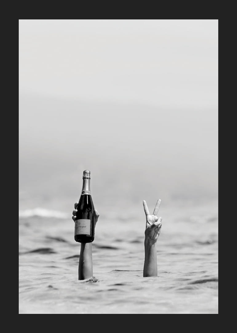 Svartvitt fotografi med två armar i vatten, en håller champagne-12