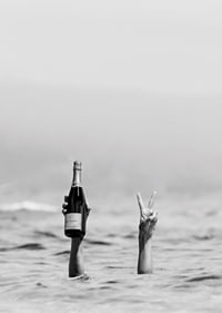 Fotografia in bianco e nero di due braccia nell'acqua, una delle quali tiene in mano dello champagne-7