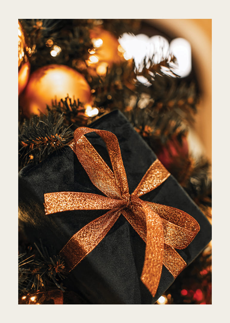 Lähikuva mustasta joululahjasta kimaltelevalla nauhalla kuusen oksien välissä-12