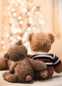 Two teddy bears from behind against bright Christmas tree, soft colors-7