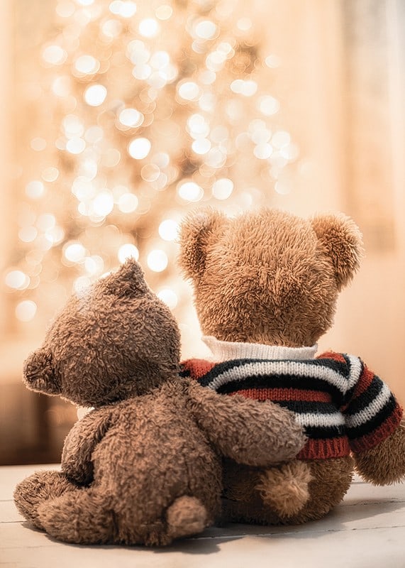 Two teddy bears from behind against bright Christmas tree, soft colors-12