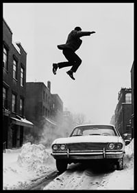 Black and white city scene with man jumping over snow-covered car-6