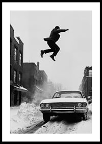 Black and white city scene with man jumping over snow-covered car-0
