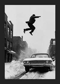 Black and white city scene with man jumping over snow-covered car-5