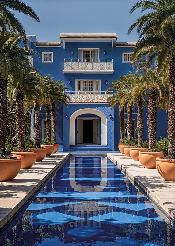 Photograph of blue villa with palm trees and long swimming pool in the foreground-12
