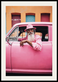 Äldre man med långt skägg i rosa bil framför färgglad fasad-2