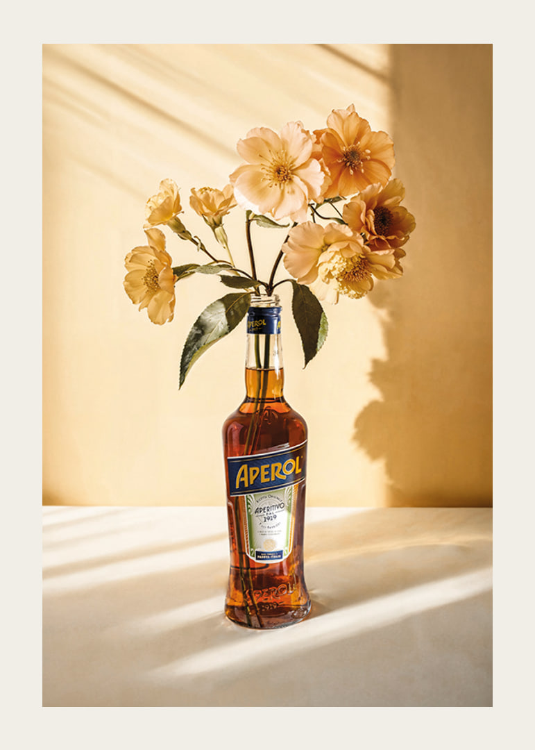 Fotografi av Aperolflaska med ljusgula blommor i soligt ljus-12