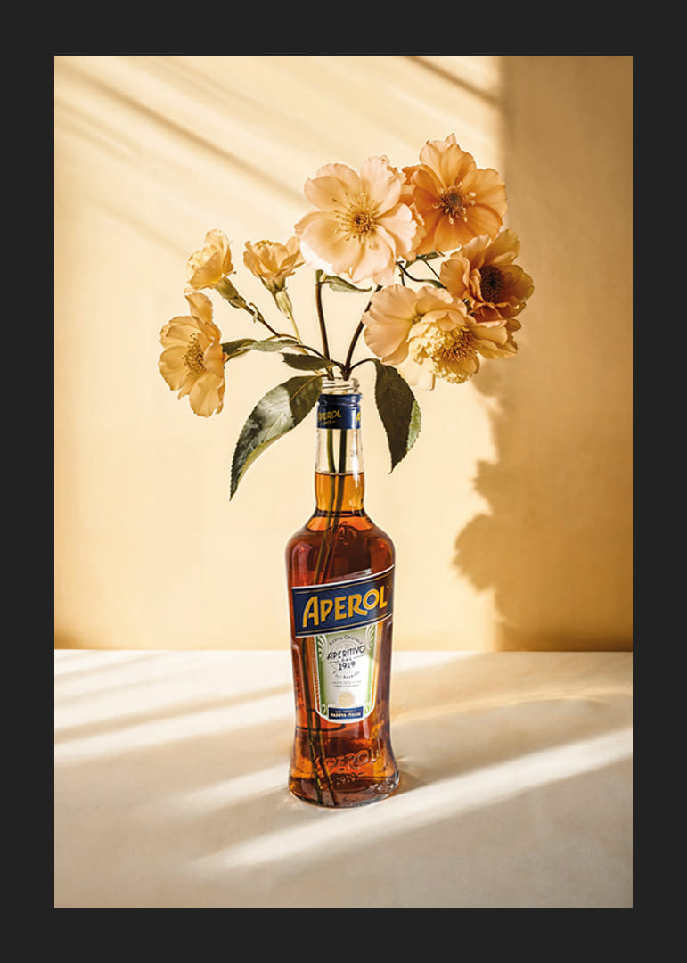 Fotografia della bottiglia di Aperol con fiori gialli brillanti in una luce soleggiata-12