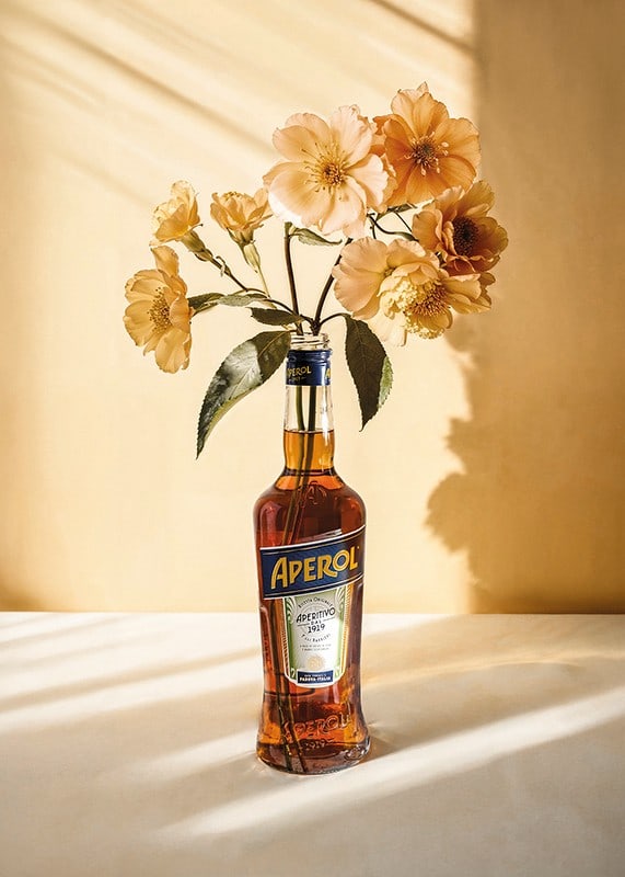 Fotografi av Aperolflaska med ljusgula blommor i soligt ljus-12