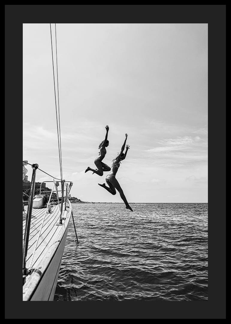 Svartvit poster med ett fotografi på två personer som hoppar från en segelbåt ner i havet-12