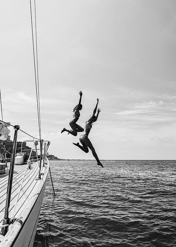 Afiș alb-negru cu o fotografie a doi oameni care sărind de pe o barcă cu pânze în mare-12