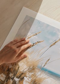 Un poster di una spiaggia assolata con erba ondeggiante, fiori selvatici e un oceano scintillante sullo sfondo-9