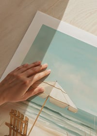 A poster of a sunny beach with a wooden chair and parasol looking out over the sea-9