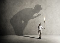 A symbolic image of facing one's inner demons, where a small torch casts a large, confrontational shadow-7